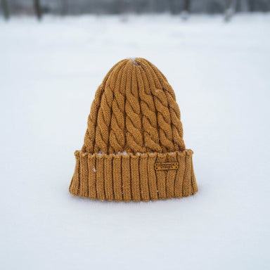 A mustard yellow cable-knit beanie hat standing upright in a snowy outdoor setting.