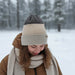 A ribbed knit beanie hat with a color-blocked design, featuring a dark brown top section, a wide beige middle section, and a light beige cuff. A small brown leather patch on the cuff reads 'HANDMADE STORIES'.