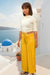 A person standing in a scenic location wearing mustard yellow adjustable wrap trousers with handwoven Andean motifs, paired with a light-colored top.
